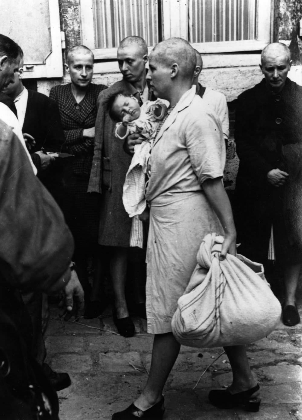 A French woman collaborator and her baby, whose father is German, tries to return to her home followed by a throng of taunting townspeople after having her head shaven following the capture of Chartres by the Allies, August 1944. It appears that she is passing some women who suffered a similar fate.
