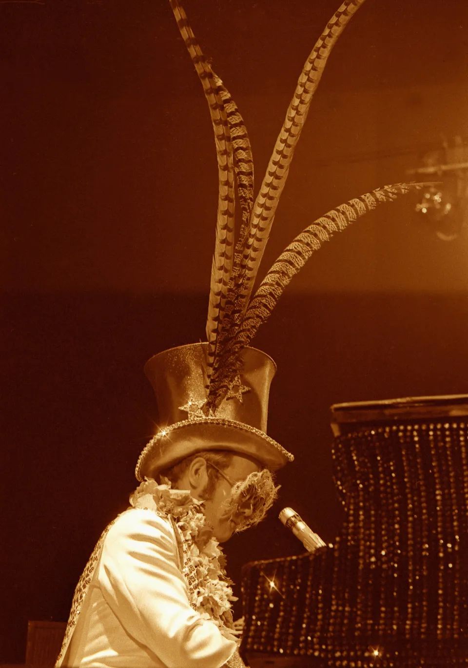 John performs onstage in a feathered hat, 1974