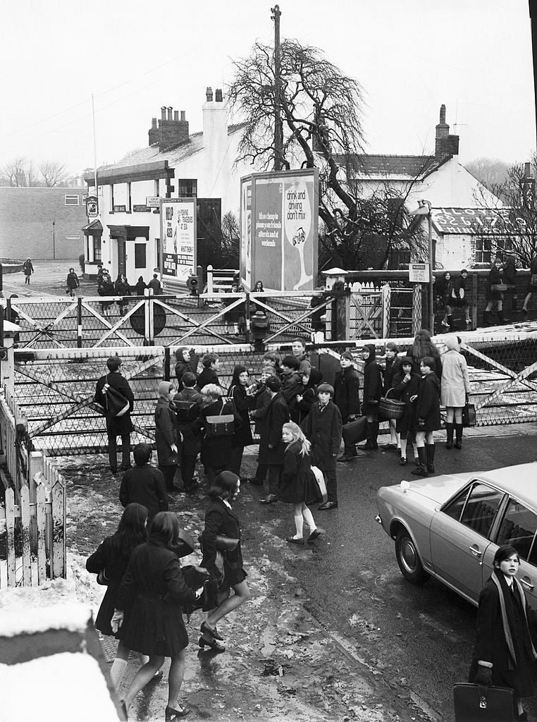 Children on the way home from school wait to cross over the railway, 1970s.