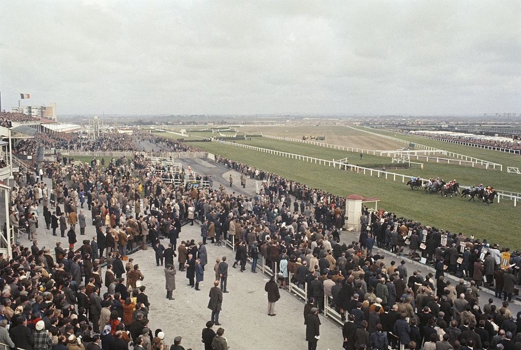 View of race goers and spectators watching a National Hunt horse race from the grandstand on the day of the Grand National steeplechase race at Aintree racecourse, Liverpool, April 1970.