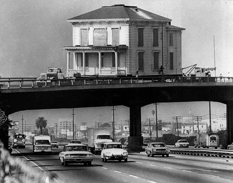 An early 1900s house crossing over the Nimitz Freeway in Oakland stops so workers can free its eaves from being entangled with a light pole. Oct. 22, 1973