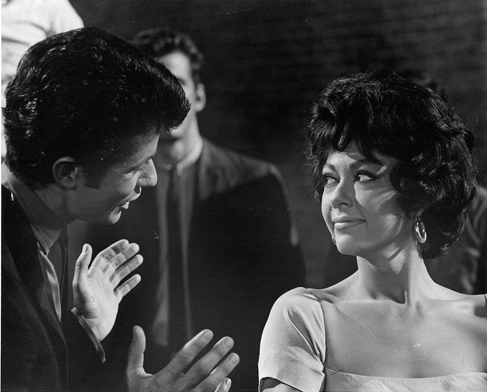 Rita Moreno Listens While George Chakiris Speaks With Her In A Scene