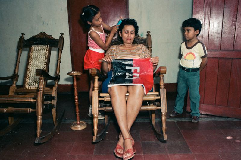 Angela's daughter Anna polishes shoes with black paint while her mother and grandmother talk, Managua, Nicaragua, 1985