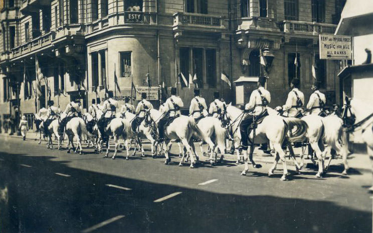 Mounted Egyptian Police passing a sign saying "H.B.M.'s and Imperial Forces. Music for all ranks"