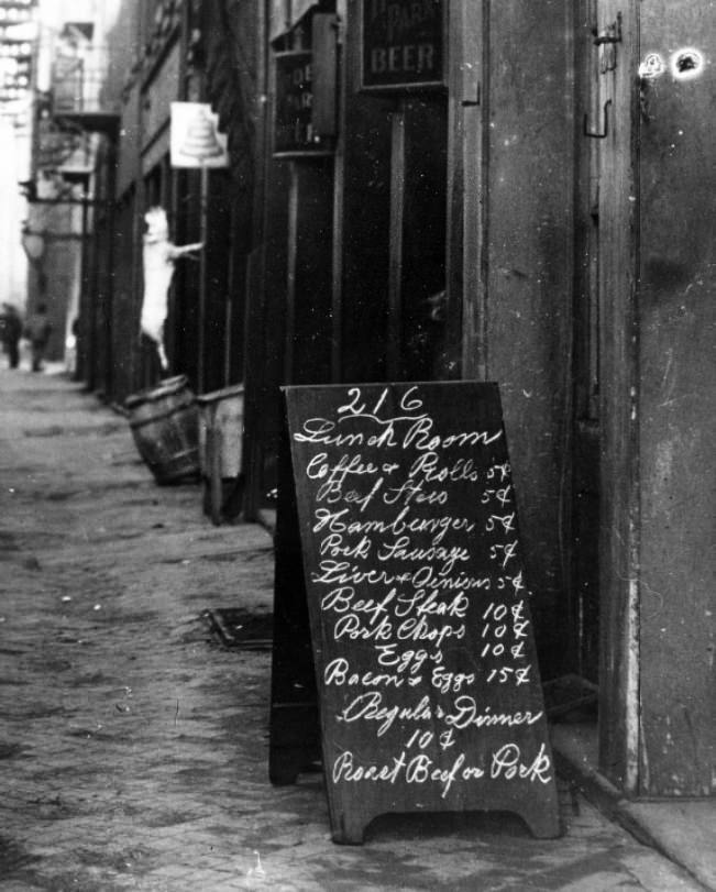 Menu sign board on sidewalk in front of restaurant. Menu items with prices are visible, 1900