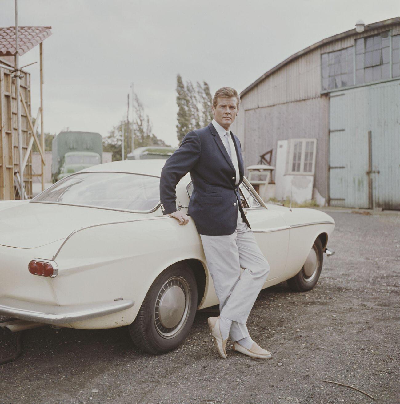 English actor Roger Moore, standing beside a Volvo P1800 car at Elstree Studios in England in 1962.