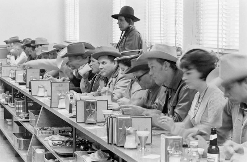 WIth a commisary counter full of movie extras clad as cowboys. lone Native American extra Iron Eyes Cody stands waiting for a seat during lunch break in filming of a Western TV show at Universal Studios, 1963.