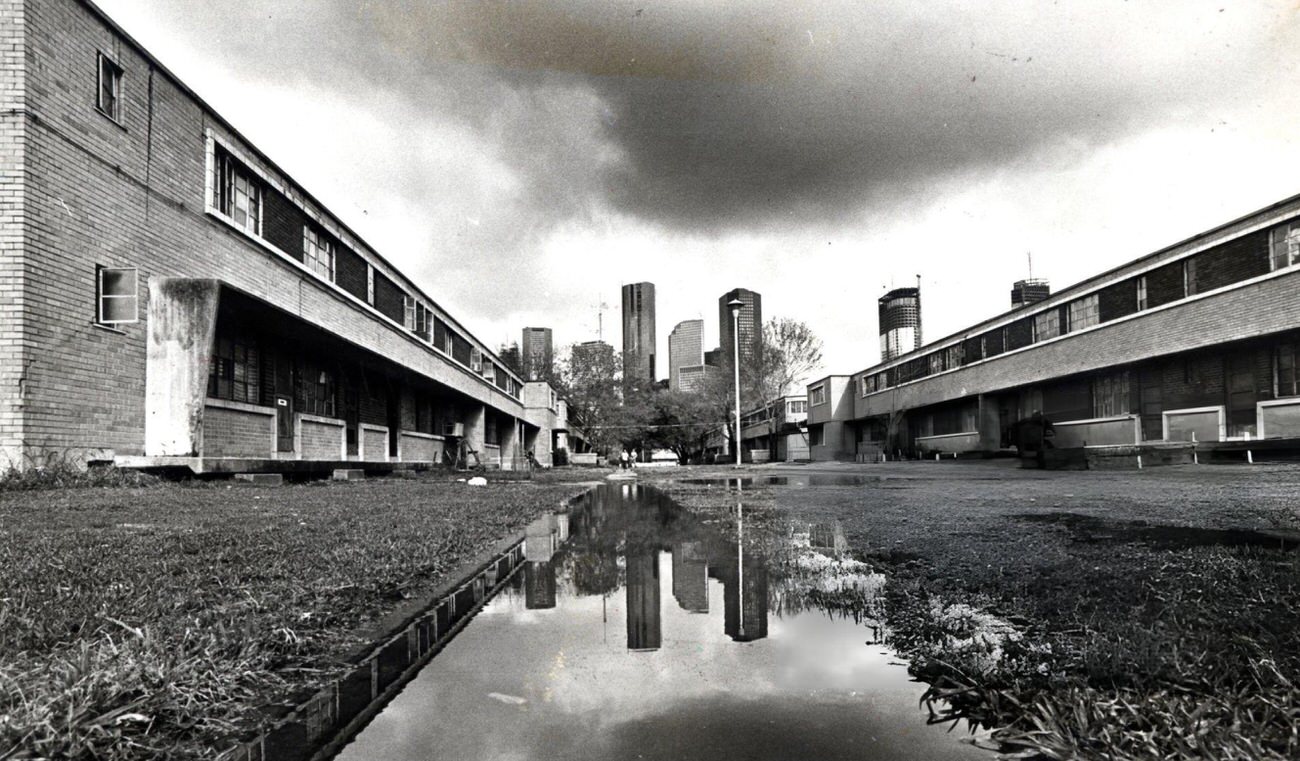 Houston skyline reflected in a puddle at Allen Parkway Village, Houston, Texas, 1983.