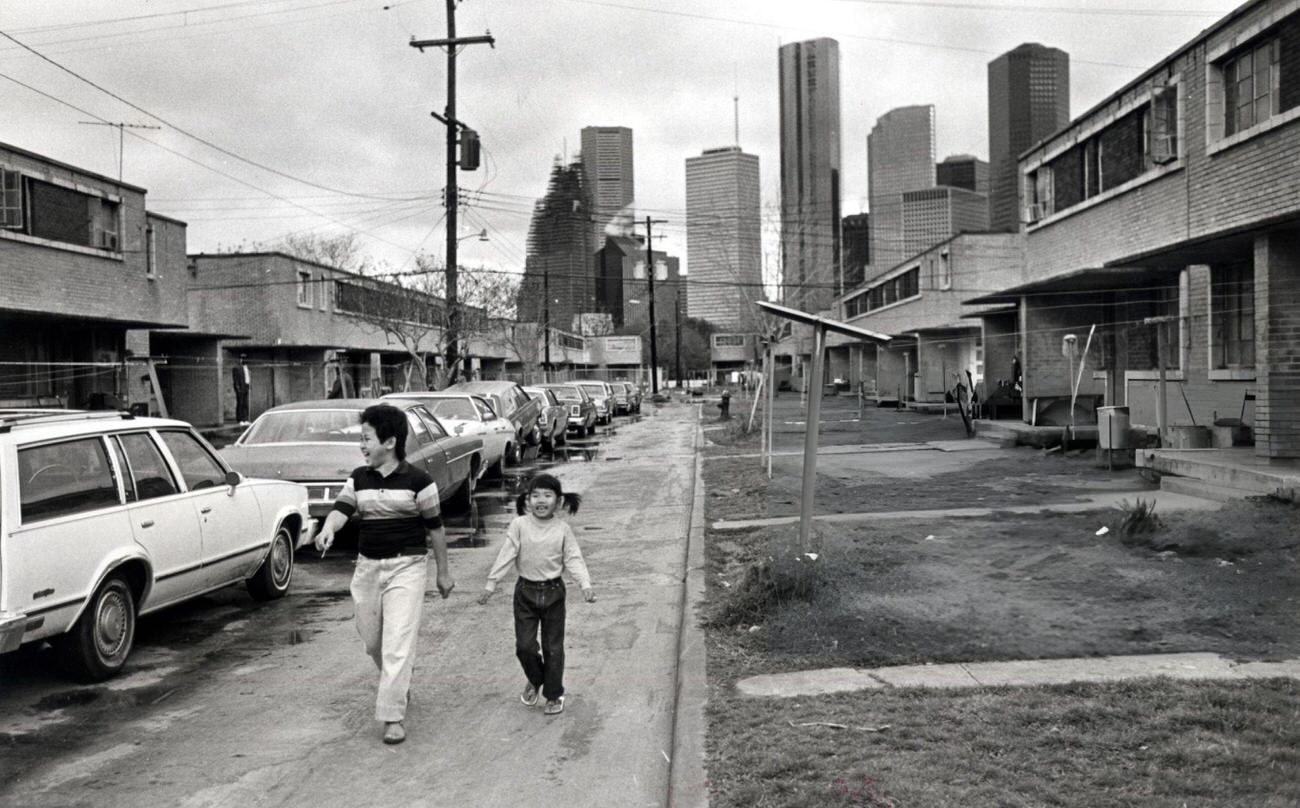 Sinh Thang and Anh Bich Tin walk between rows of apartments in Allen Parkway Village, Houston, Texas, 1983.
