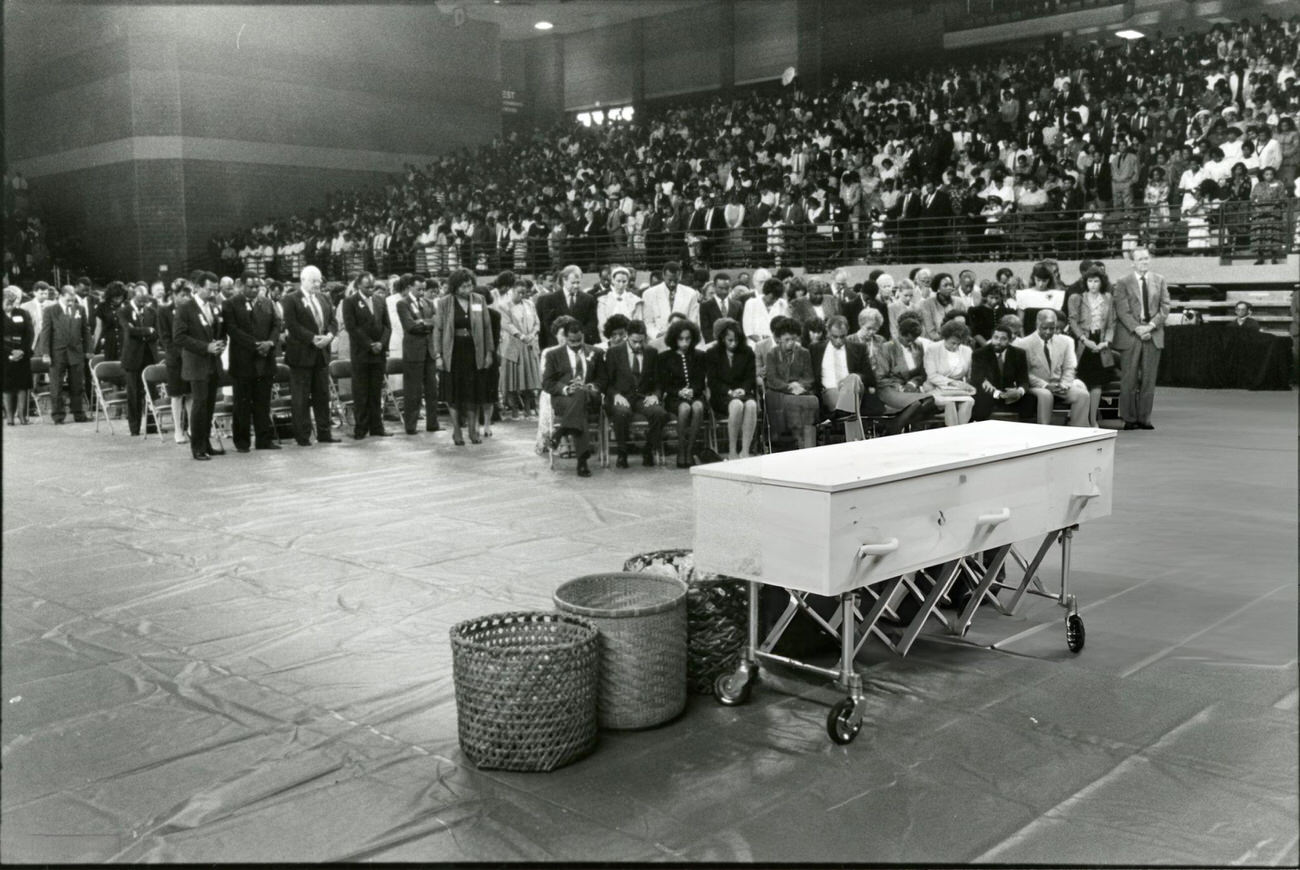 Family and friends of Mickey Leland attend his memorial service at Texas Southern University with an empty pine casket, Houston, Texas, August 18, 1989.