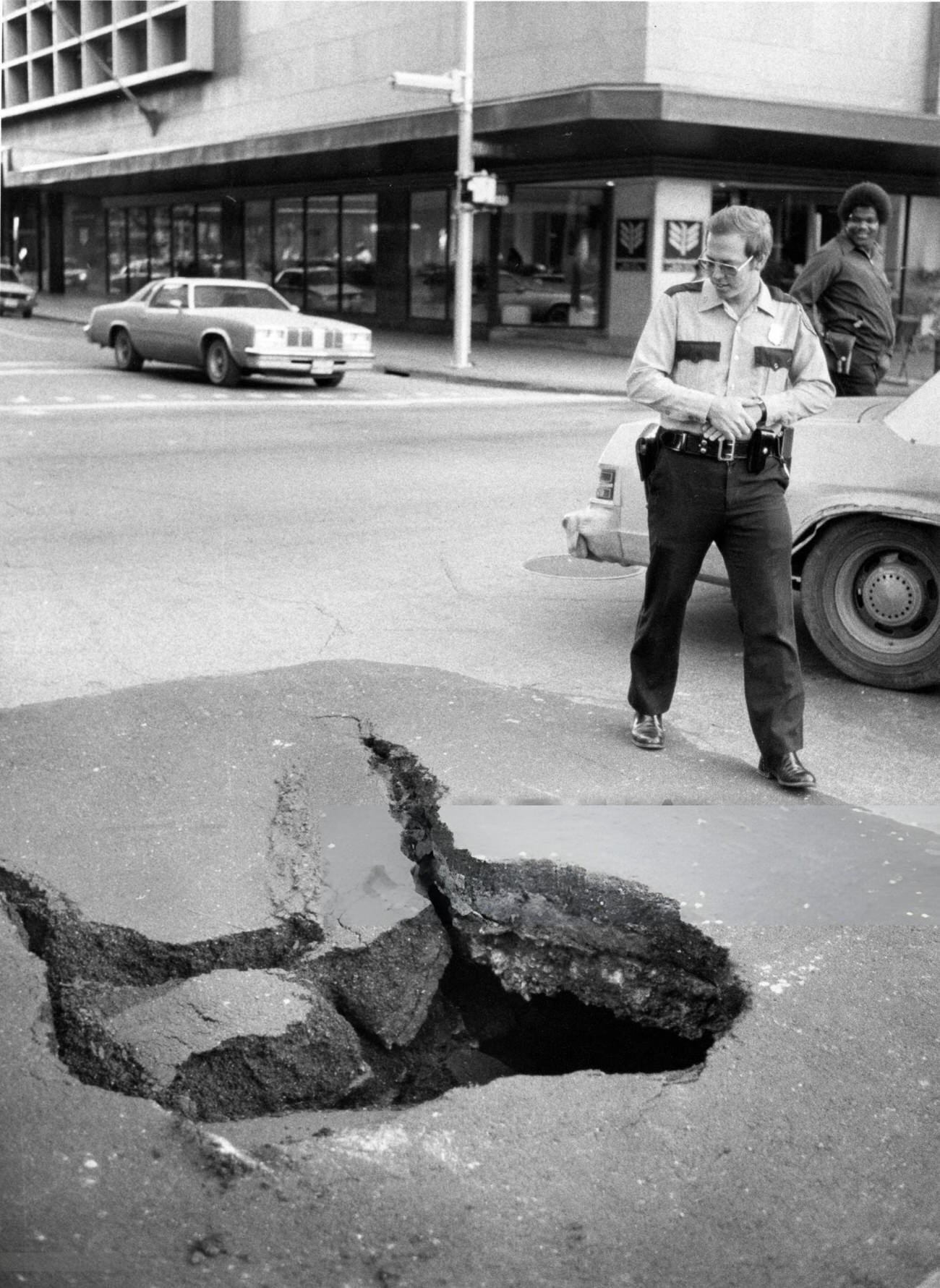 HPD Officer W.T. Howard inspects a "street cave" caused by a leaking water main at Travis and Polk, near the Houston Natural Gas Building, 1980.