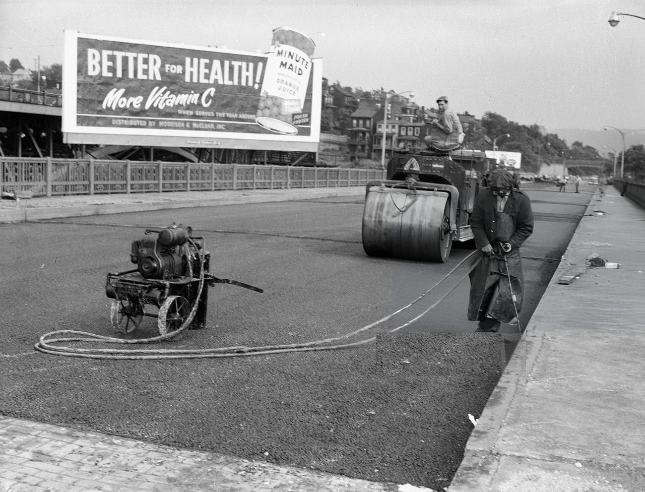 Two men paving a road with a steam roller, with a Minute Maid orange juice billboard in the background, 1960s