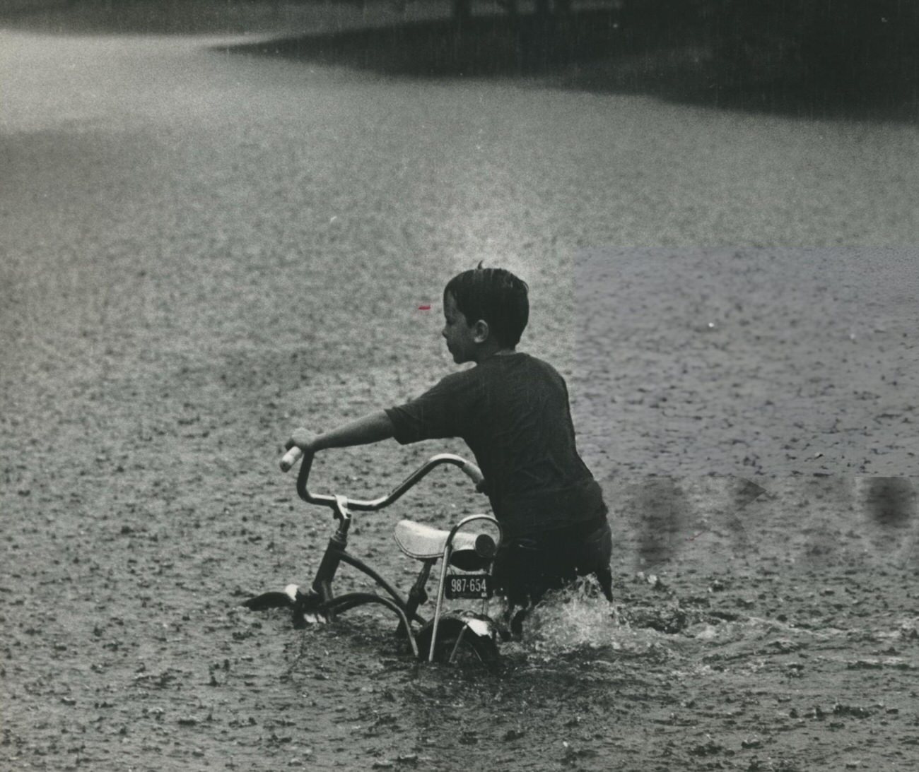 A boy navigates floodwaters on his bicycle in Houston, Texas, 1970.