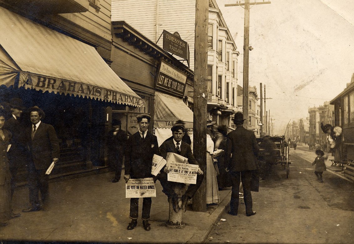 Pete Rielly and Eddie Campi selling newspapers in front of Abraham's Pharmacy, 1198 McAllister Street, at Fillmore, 1909.