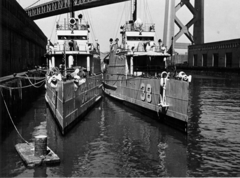 Two ships docked at a pier near the Bay Bridge, 1940s