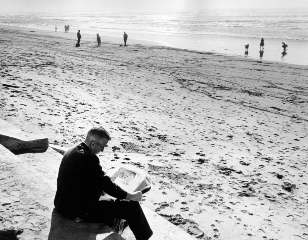 Man reading a newspaper at Ocean Beach, 1960.