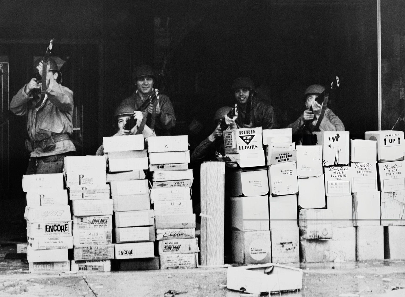 Soldiers of the National Guard shelter behind a stack of boxes