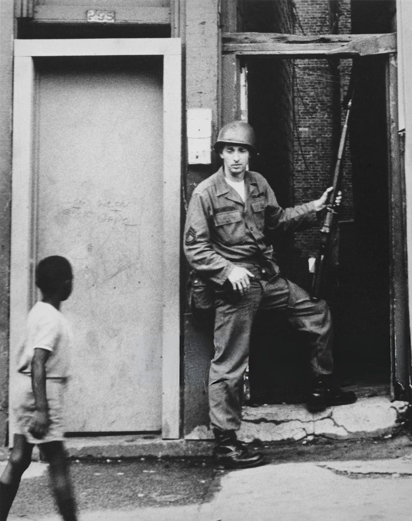 A young African American boy passes a National Guardsman in an alley of Springfield Avenue
