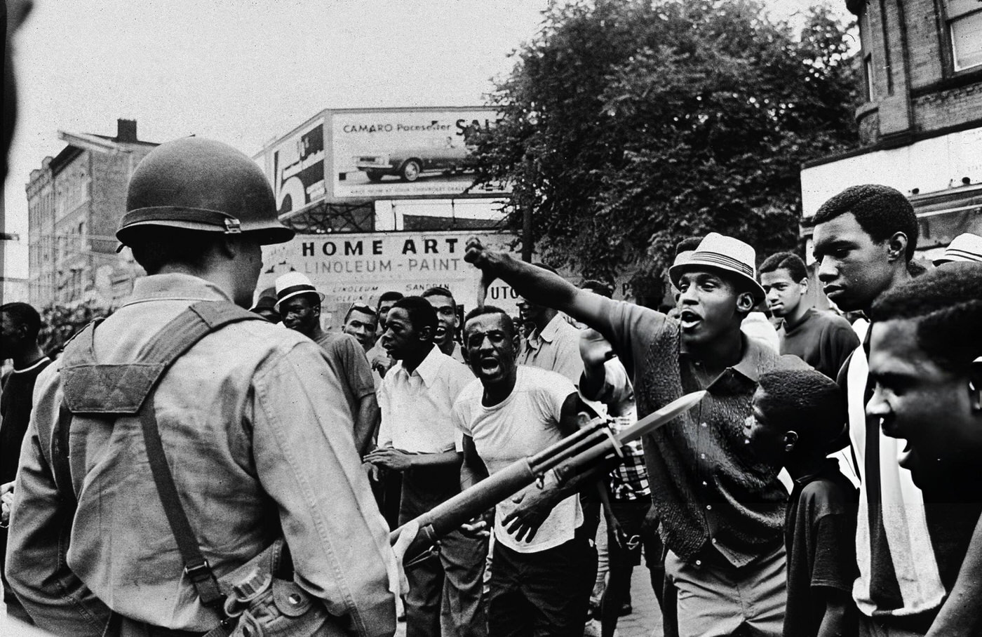 A Black man gestures with his thumb down to an armed National Guardman, during a protest
