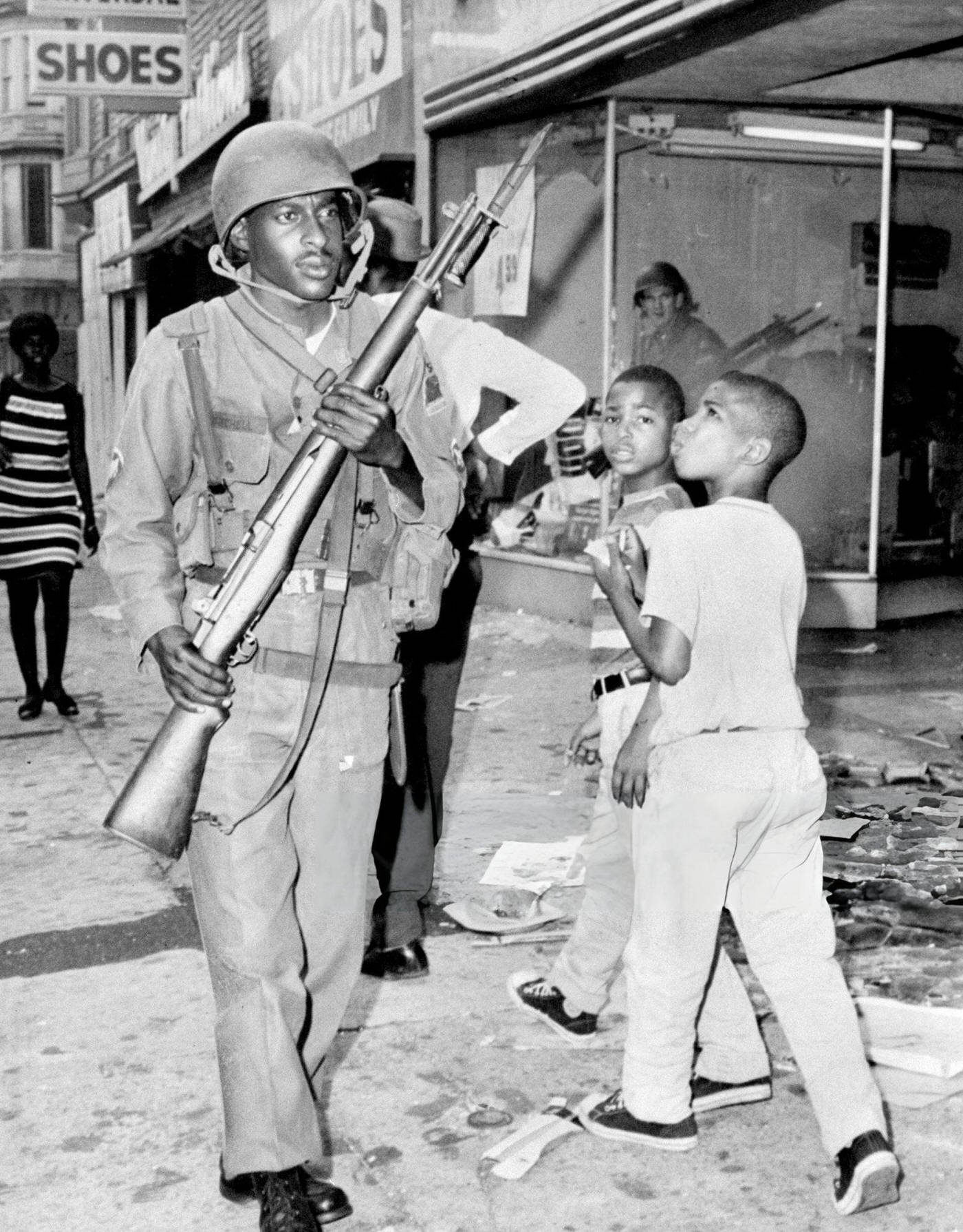 Newark children pass National Guardsman during riots, 1960s.