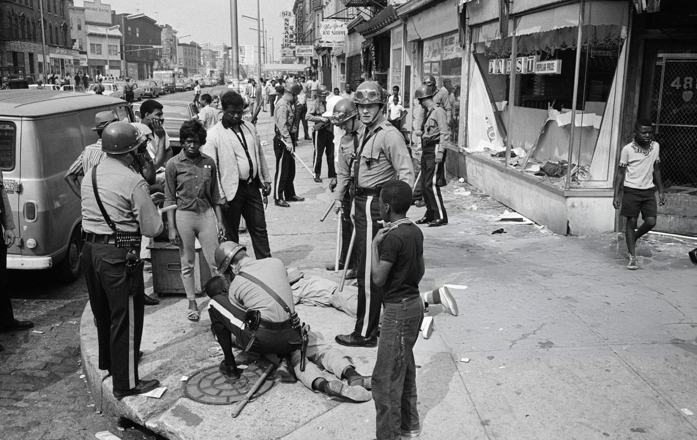 Police officers and National Guardsmen round up looters on a major thoroughfare following a second night of rioting in Newark, New Jersey, 1960s.