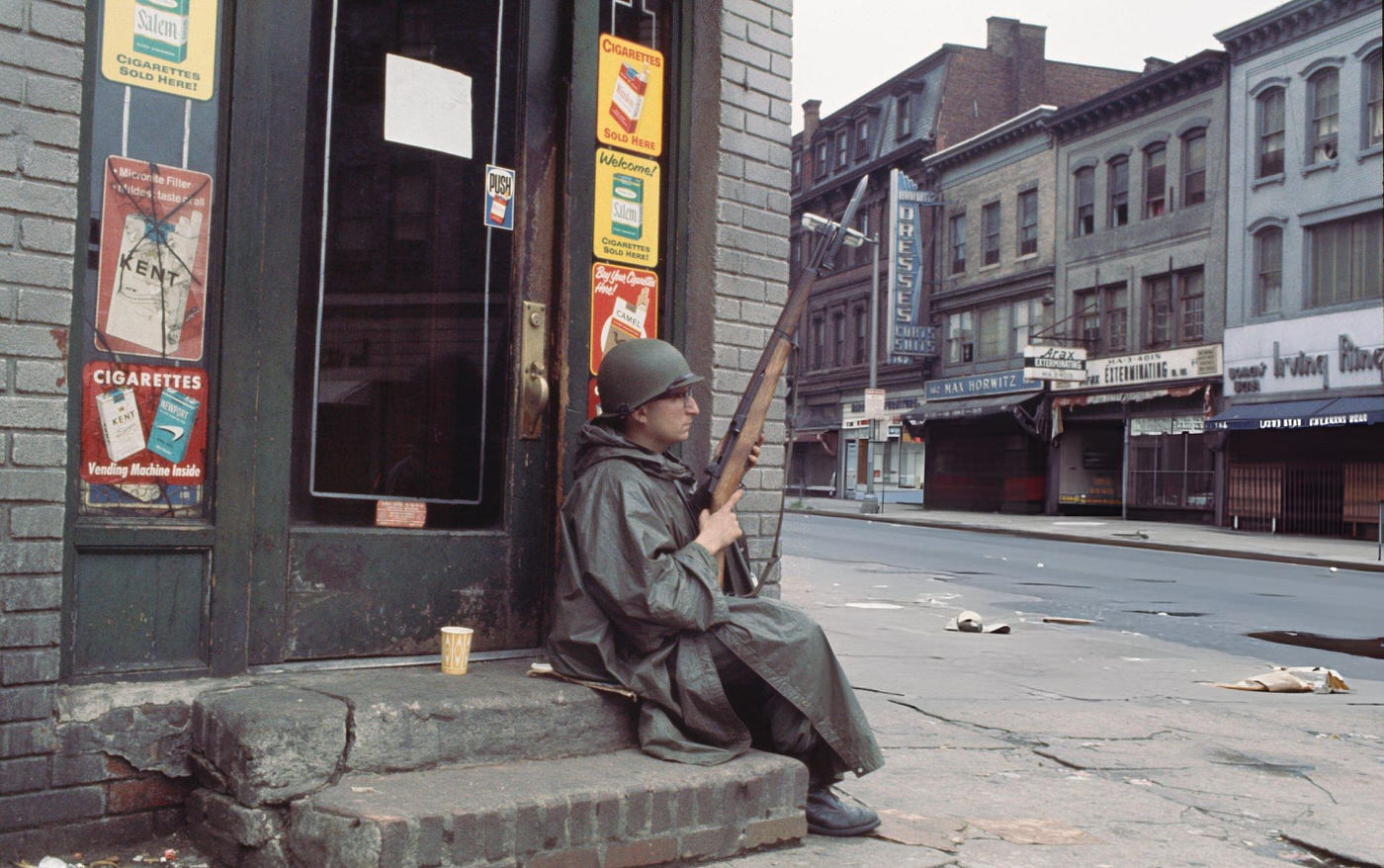 A member of the National Guard sits with his rifle on the steps of a closed convenience store