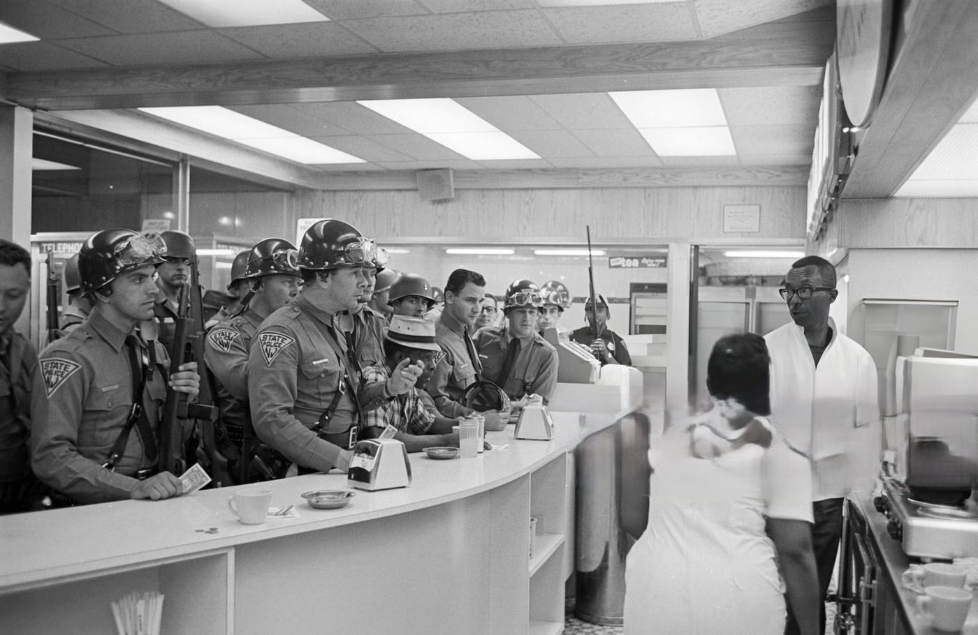 State Police officers in uniform and armed are at the counter in a cafeteria, among them an elderly African-American man