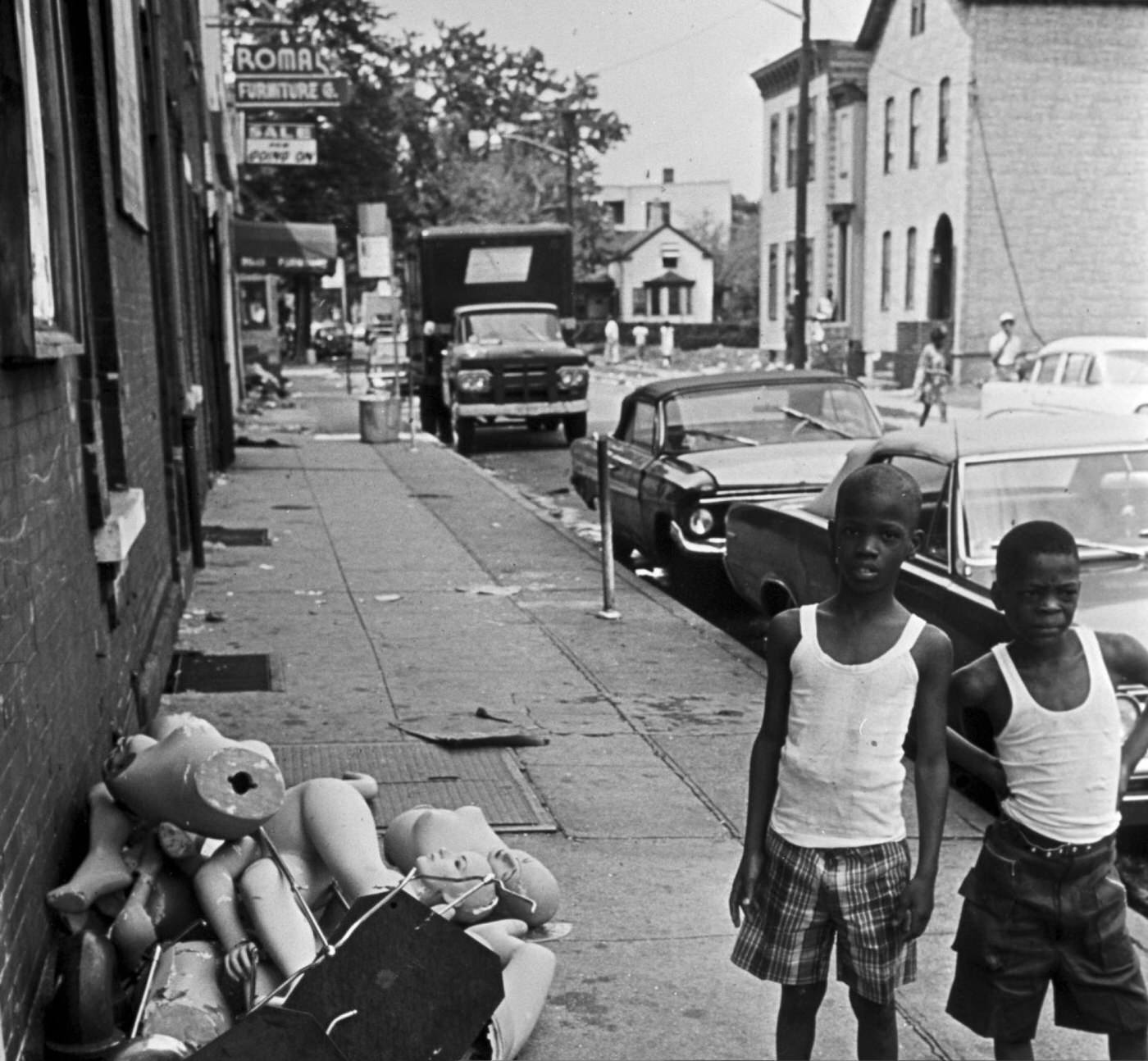 Two young African American boys in t-shirts and Bermuda shorts near broken mannequin busts on the sidewalk