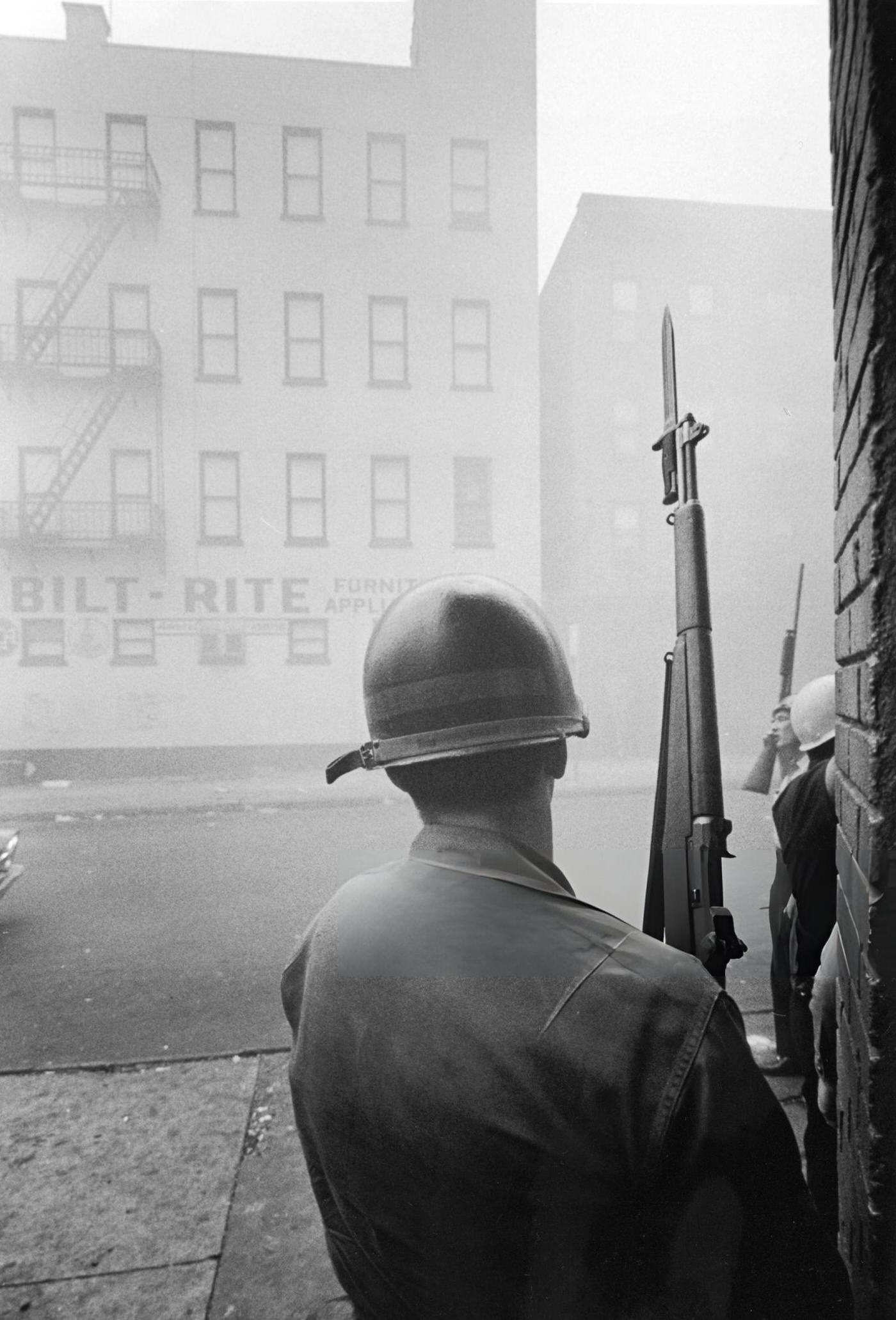 A National Guardsman stands behind a corner and holds a Garand rifle