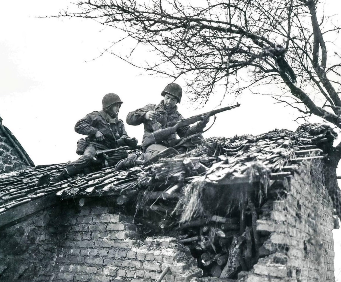 S/Sgt. Urban Minicozzi and Pfc. Andy Masiero stop to reload while sniping snipers from the roof of a building in Beffe, Belgium, 1945.