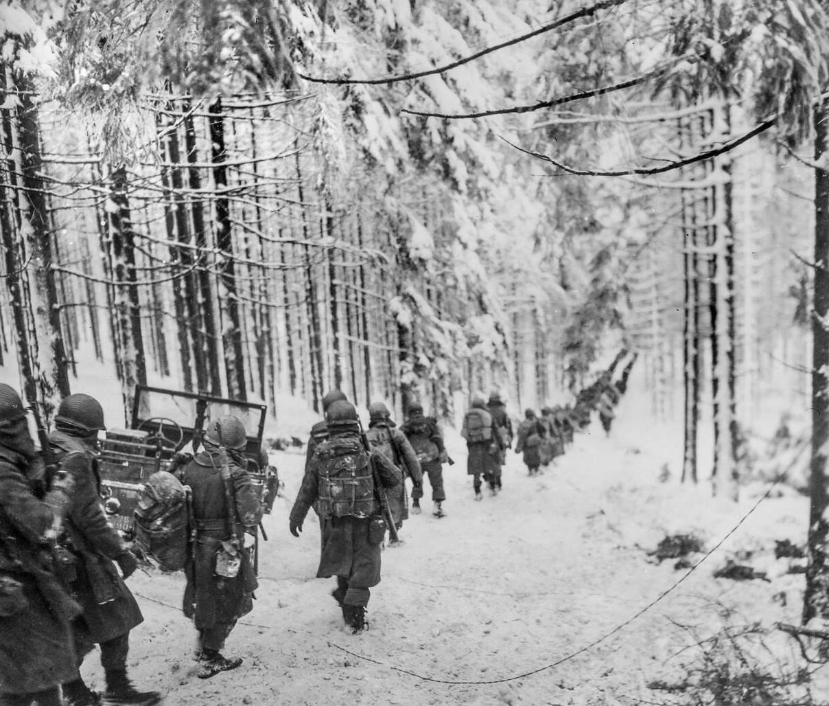 American infantry troops soldiers of the 289th Infantry Regiment march along the winter snow-covered road on their way to cut off the Saint Vith-Houffalize road in Belgium, 1945.