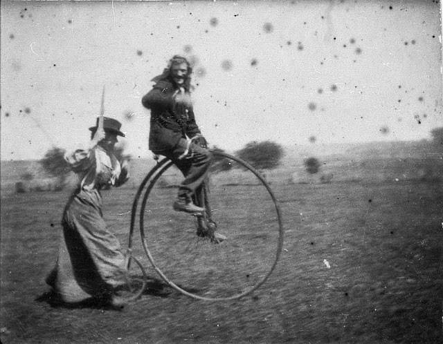 A man on a penny-farthing bicycle being chased by his sister, 1900.