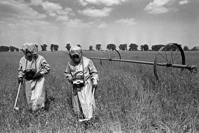 May 1986: In the 30km no-go zone around the reactor, liquidators measure radiation levels in neighboring fields using antiquated radiation counters, wearing anti-chemical warfare suits that offer no protection against radioactivity, and “pig muzzle” masks. The young plants will not be harvested, instead used by scientists to study genetic mutations in plants.