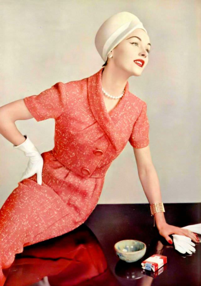 A model in a coral speckled tweed two-piece, a very short jacket with a criss-cross neckline and short sleeves, by Pierre Balmain, 1957.