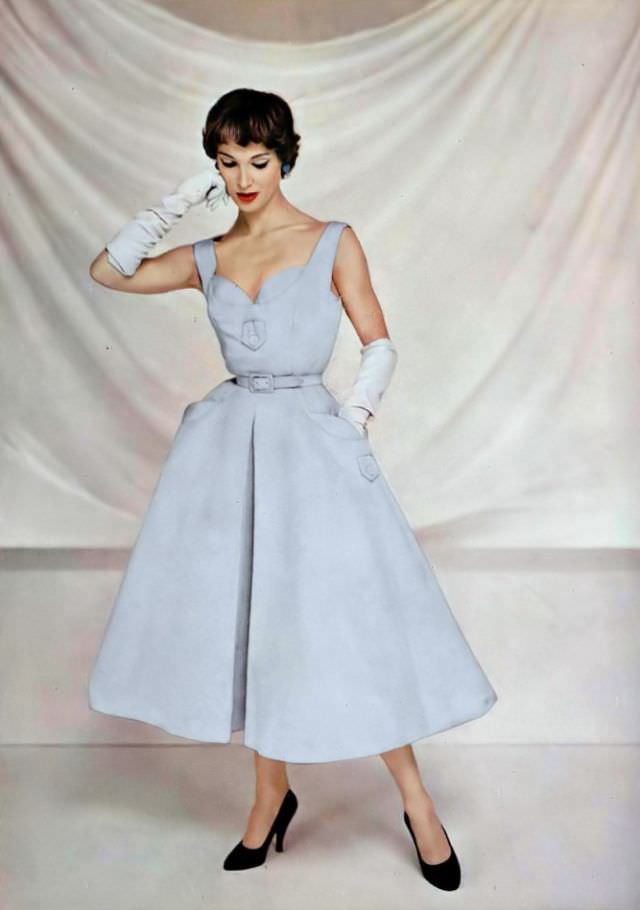 Ann Farrar in a pale blue ottoman dress, the bodice has buttoned tabs as do the pockets, the skirt is wide with an inverted pleat, by Pierre Balmain, 1954.