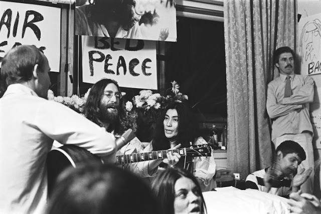 The couple sits among friends Tommy Smothers, far left, and Derek Taylor, standing far right, singing "Give Peace a Chance."