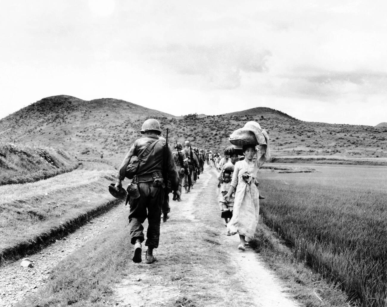 During the Korean War, a line of US Army soldiers file past a group of Korean women and children, 1950s.