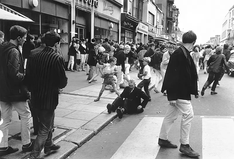 An old man falls to the ground caught in a street fight between mods and rockers in Hastings, England, 1964.