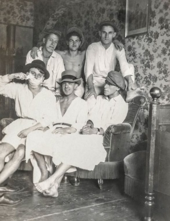 Man shaving his face while his friends sit in their pajamas