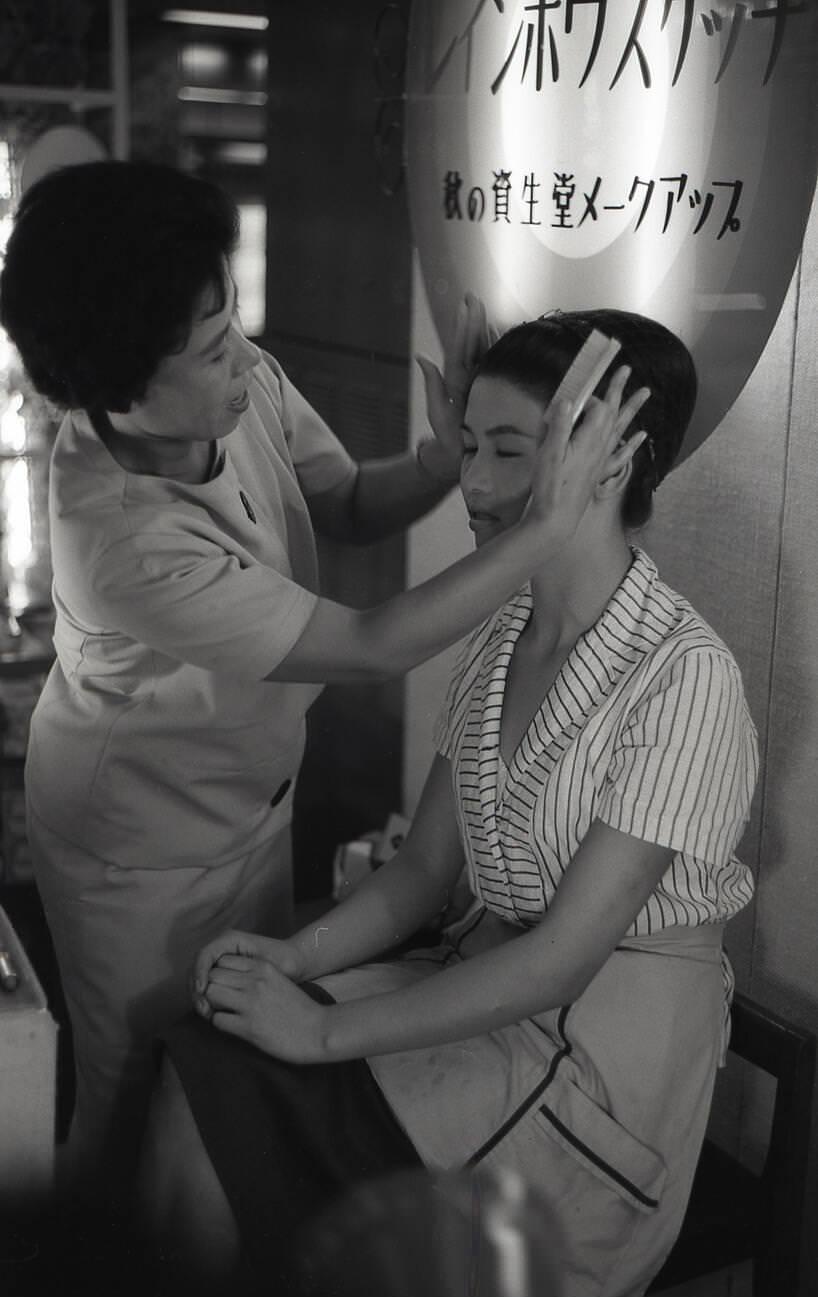 A Shiseido make-up artist touches the face of a young woman during a make-up demonstration, 1958.