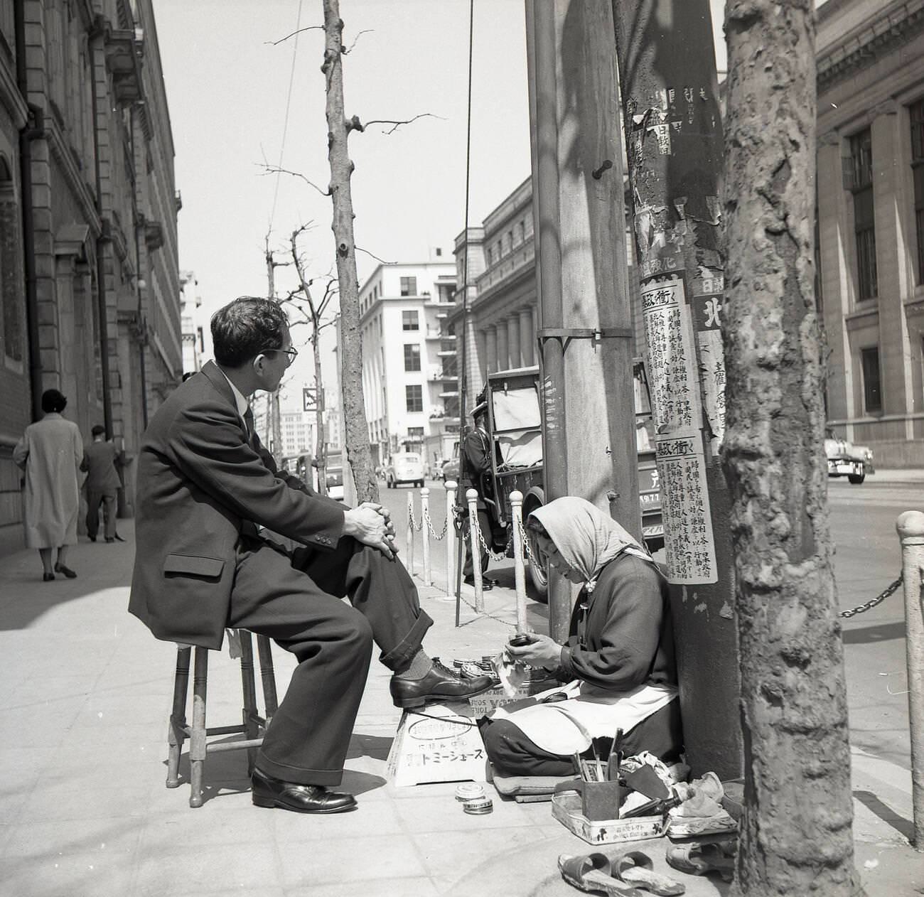 A Japanese businessman sitting outside on a stool having his shoes shined, 1950s.