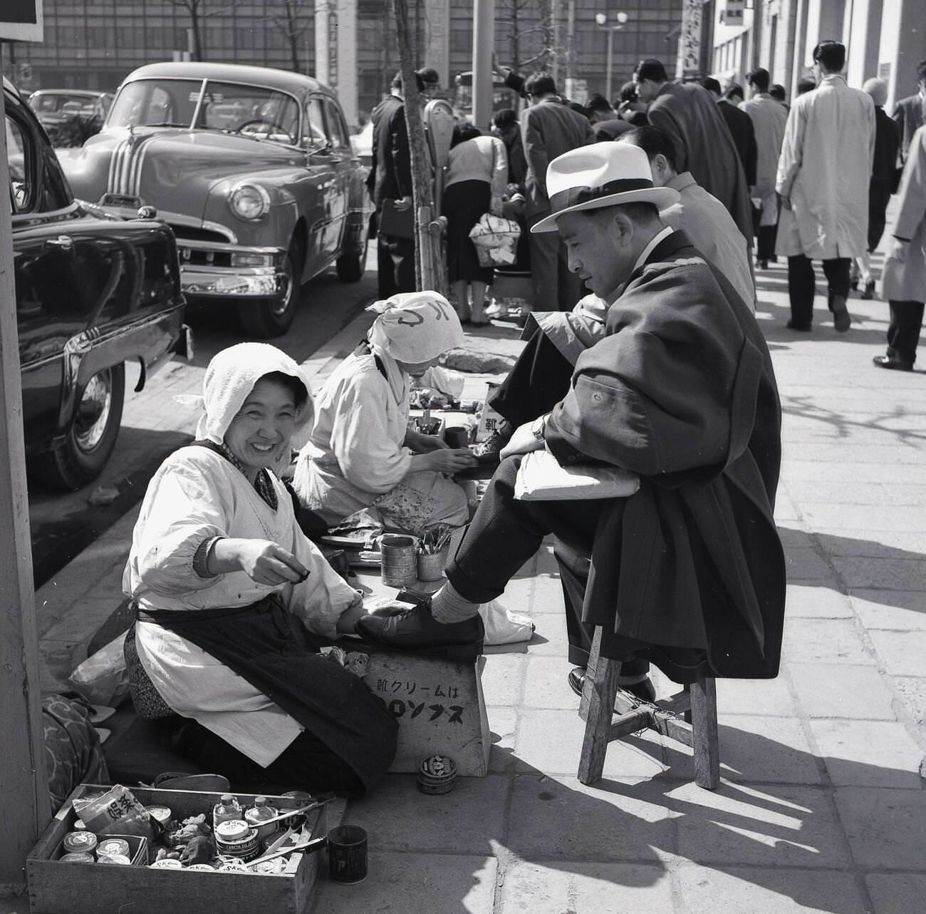 Japanese business men sitting on stools getting a shoeshine outside, 1950s.