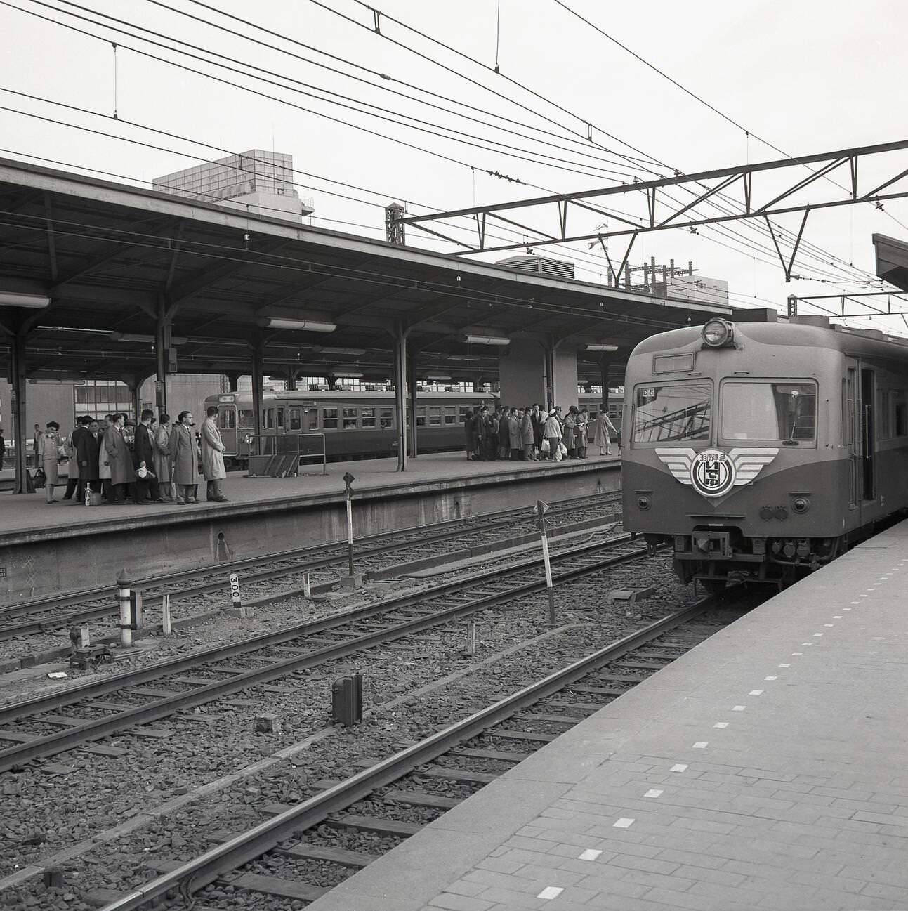 An overground train arrives on one platform, while Japanese rail commuters wait for their train to arrive, 1950s.