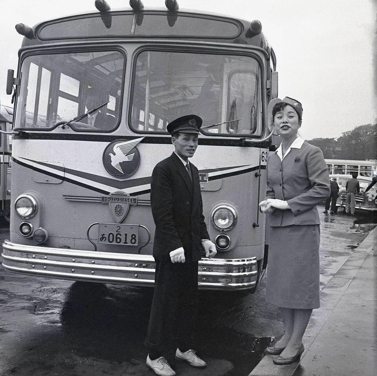 Uniformed male and female guides stand outside a parked up Isuzu tourist bus, 1950s.