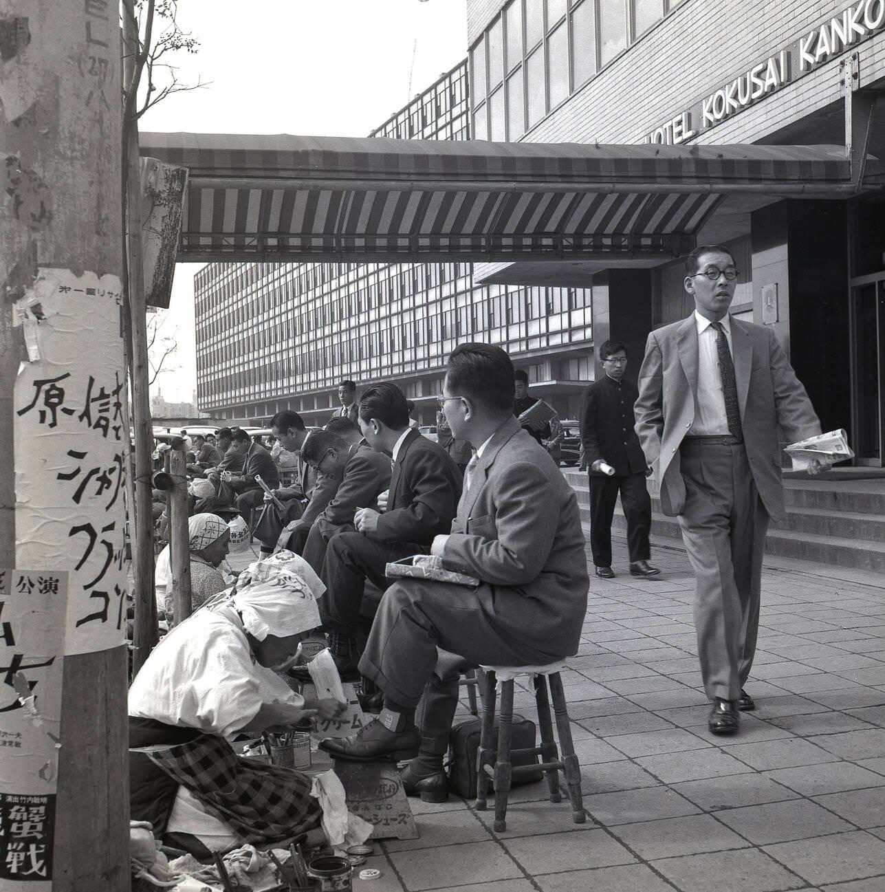 Japanese businessmen sit on little stools having their shoes polished and cleaned, 1950s.