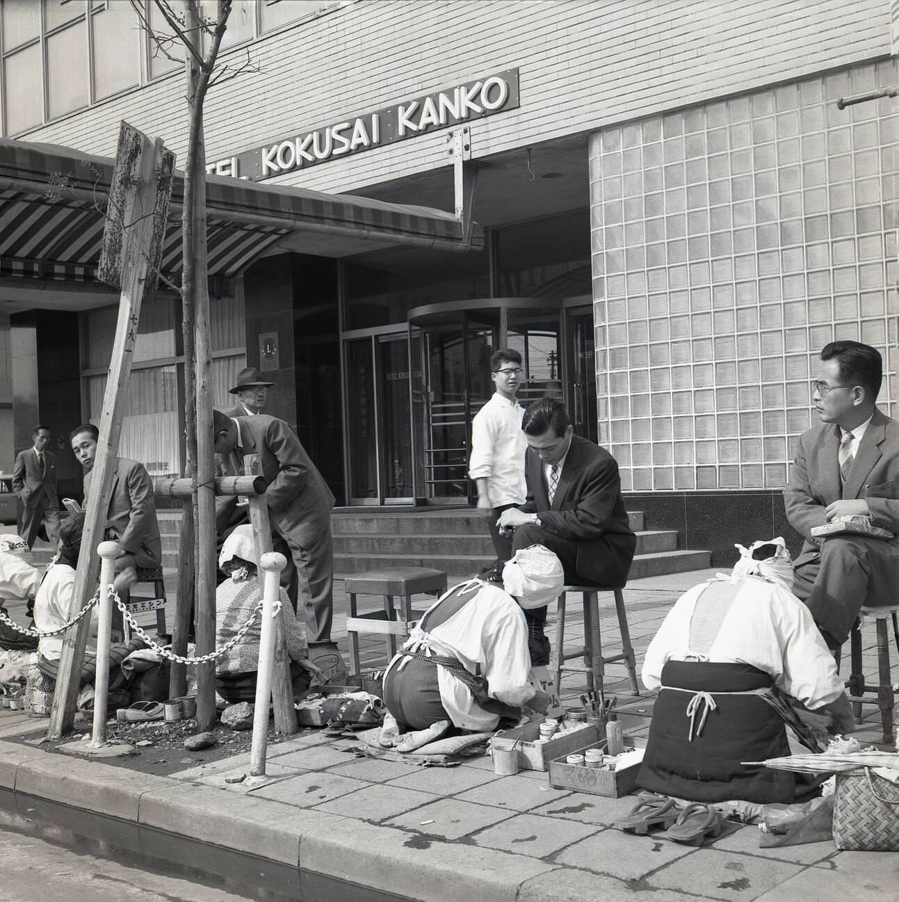 Japanese businessmen sit on little stools having their shoes polished and cleaned, 1950s.