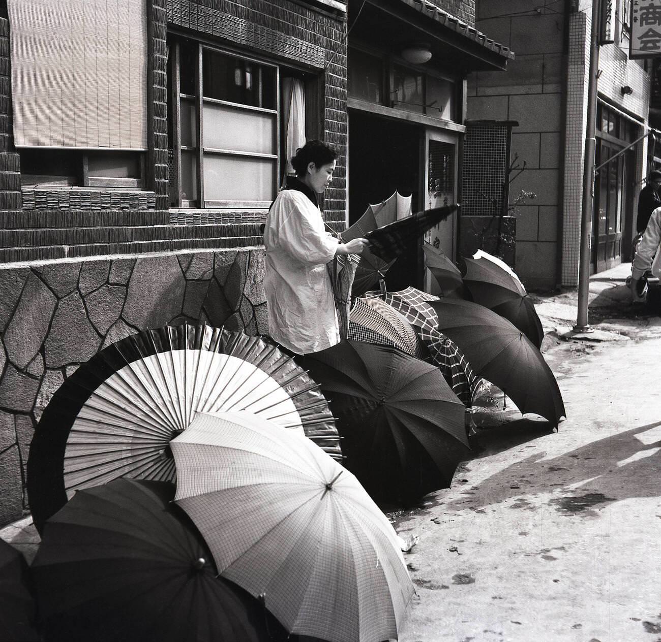 A female Japanese street trader outside a building selling umbrellas in Tokyo, 1950s.