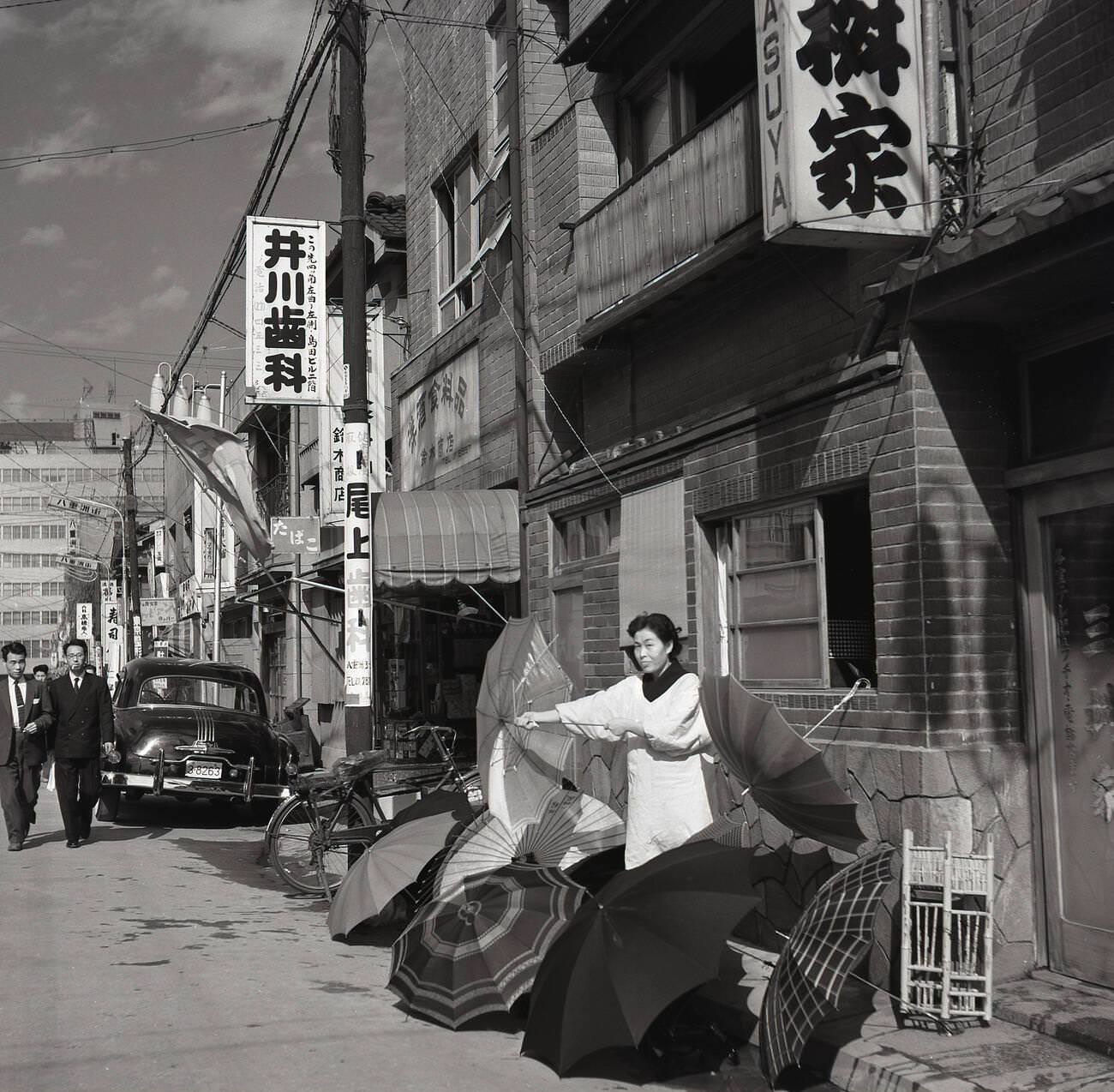 A female Japanese street trader outside a building in the old town selling umbrellas in Tokyo, 1950s.