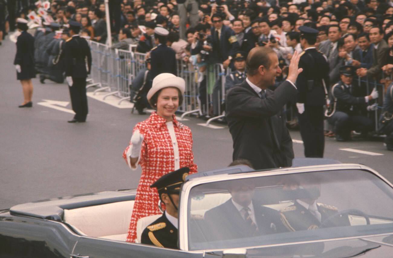 Queen Elizabeth II and Prince Philip, Duke of Edinburgh wave to cheering crowds as the Royal couple proceed in a motorcade in Tokyo.