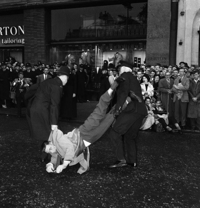 A well-dressed man is dragged away, head down, by police officers after sitting down during the huge Ban-the-bomb rally in London's rain-soaked Trafalgar Square, United Kingdom, 1961.